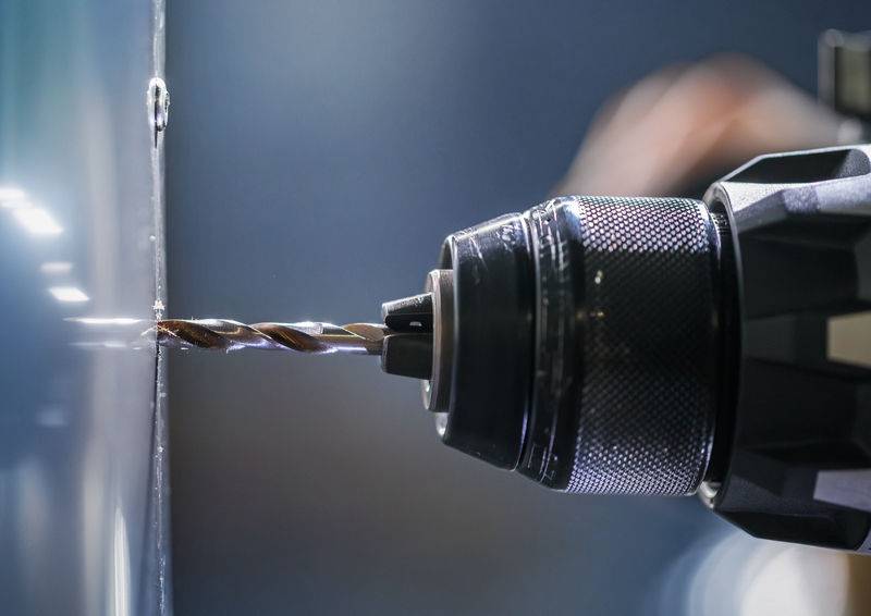 Nahaufnahme einer Elektrobohrmaschine mit einem Metallbohrer, der in eine reflektierende Metalloberfläche bohrt und die Präzision bei industriellen Arbeiten zeigt.