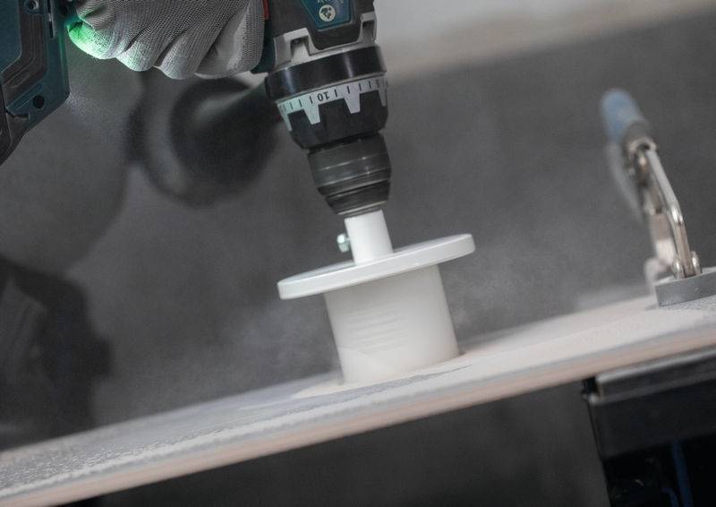 Eine Person benutzt eine Elektrobohrmaschine mit einem Lochsägen-Aufsatz, um ein kreisförmiges Loch in ein Stück Holz zu schneiden, was eine Heimwerkeraufgabe zeigt.