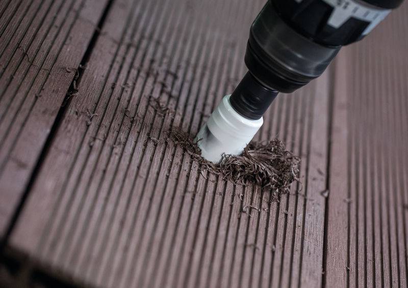 Ein Bohrer mit einem Lochsägebit schneidet in eine strukturierte braune Holzoberfläche und erzeugt Holzspäne.