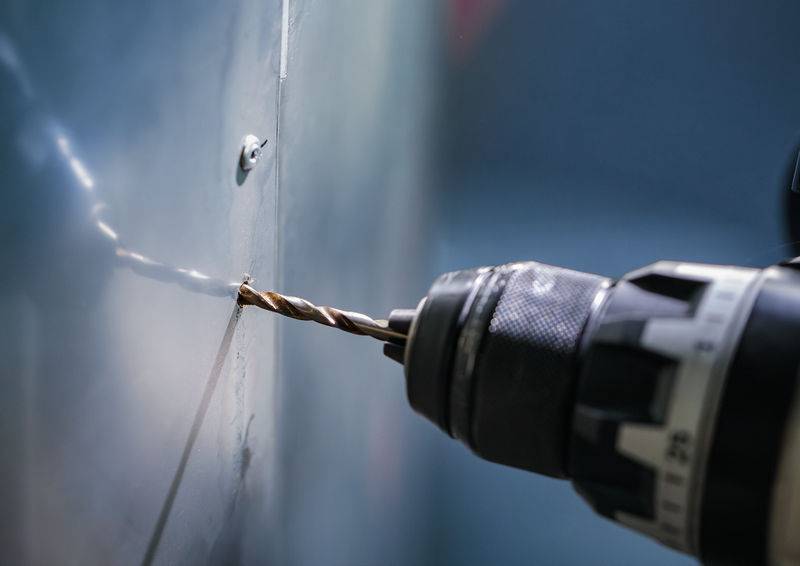 Eine Großaufnahme einer Bohrmaschine in Aktion, die ein Loch in eine Metalloberfläche bohrt, mit Fokus auf die präzise Arbeit an einem glatten, reflektierenden Panel.