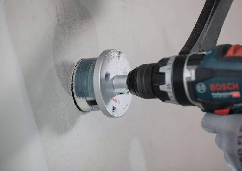 Ein Elektrobohrer schneidet mit einer Kreissäge-Aufsatzvorrichtung in eine Wand ein und erzeugt ein sauberes Loch in der Oberfläche.