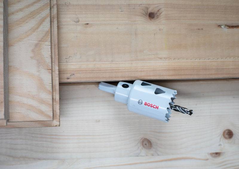 Eine Bosch-Lochsäge, die an einem Bohrgerät befestigt ist, wird in der Nähe eines Holzbretts positioniert, um bereit zu sein, ein Loch für eine Holzverbindung oder Befestigung zu schaffen.