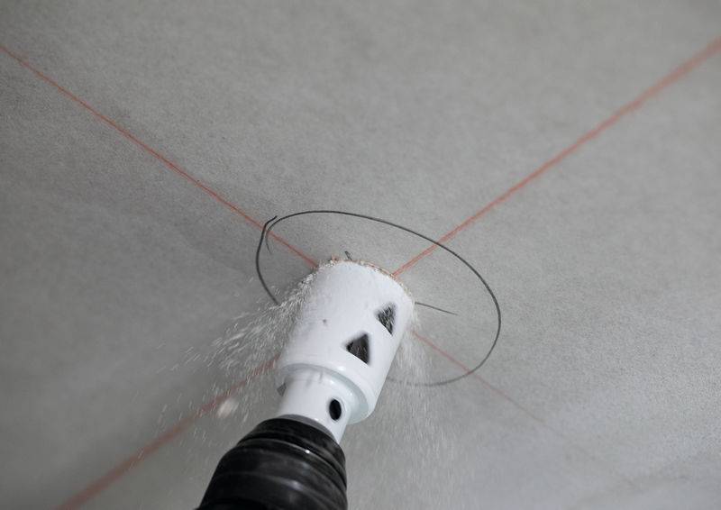 Ein Bohrer, der ein kreisförmiges Loch in einer Decke schneidet, wobei Staubpartikel dispersiert werden.