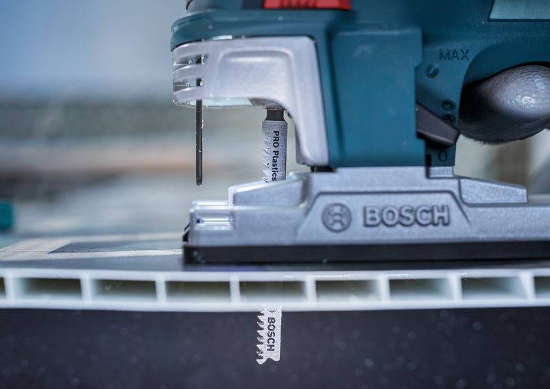 Eine Stichsäge durchschneidet ein Materialstück, mit Fokus auf den Markennamen Bosch auf dem Sägeblatt und dem Werkzeuggehäuse.