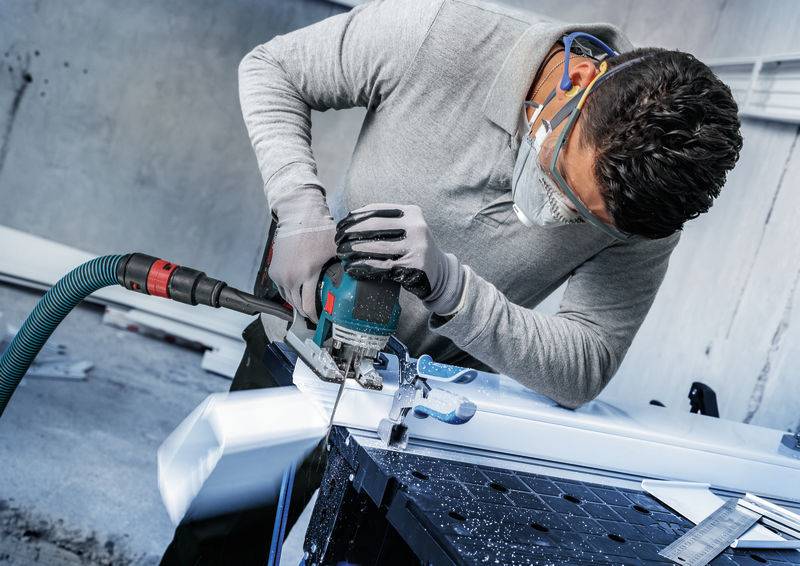 Eine Person in Schutzausrüstung benutzt ein Elektrowerkzeug, um ein Metallstück in einer Werkstattumgebung zu schneiden.