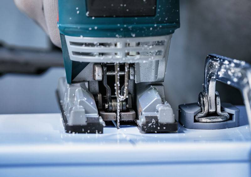 Nahaufnahme einer elektrischen Stichsäge, die durch ein Holzstück schneidet, wobei Sägespäne umherfliegen und präzise Holzbearbeitung in Arbeit zeigt.