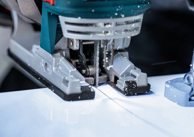 Eine Nahaufnahme einer Elektrosäge, die durch ein weißes Material schneidet, mit fliegendem Sägemehl. Das Sägeblatt ist in Bewegung und deutet auf aktives Schneiden hin.