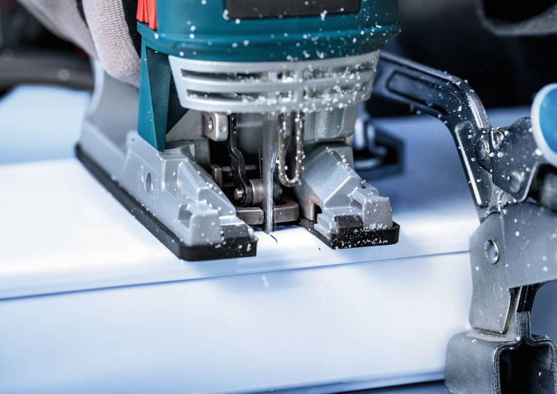 Eine Elektrostichsäge schneidet durch ein dickes Stück weißes Material, wobei Sägespäne sichtbar sind. Das Werkzeug wird ruhig gehalten und deutet auf Präzisionsarbeit hin.