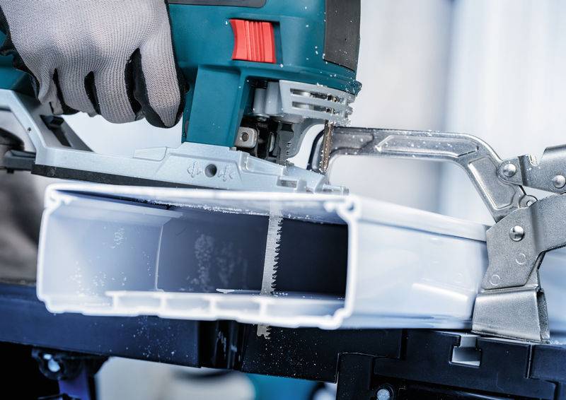 Eine Person verwendet eine Stichsäge, um ein weißes Kunststoffrohr zu schneiden, mit einer Nahaufnahme des Werkzeugs und des Materials, die eine DIY-Aufgabe hervorhebt.