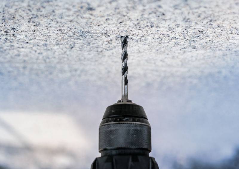 Ein Bohrmeißel, der senkrecht eine Steinoberfläche durchdringt, fotografiert aus einem flachen Winkel.