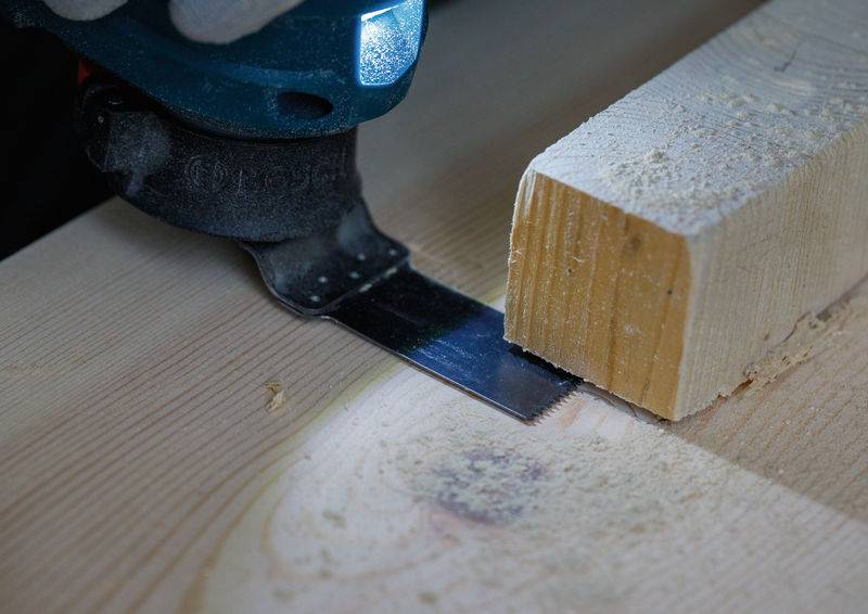 Ein Elektrowerkzeug mit einer Sägeblatt schneidet durch ein Holzstück und zeigt Holzspäne und eine glatte Schnittfläche.