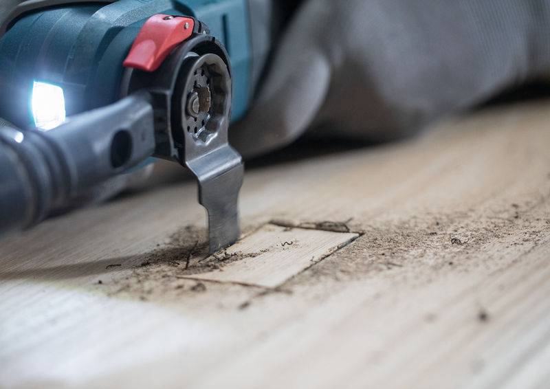 Eine Nahaufnahme eines Elektrowerkzeugs, das ein rechteckiges Stück aus einer Holzoberfläche schneidet, wobei Sägespäne den Bereich umgeben.