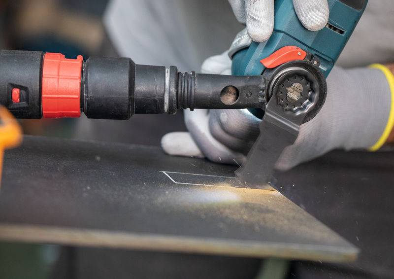 Eine Person mit Handschuhen benutzt ein Elektrowerkzeug, um eine rechteckige Form in einem Metallblech zu schneiden und erzeugt dabei Funken.