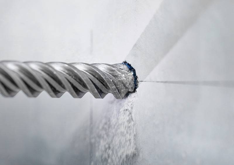 Ein Bohrer, der in eine weiße Wand eindringt, erzeugt Staub und veranschaulicht den Prozess des Bohrens für Bau- oder DIY-Aufgaben.