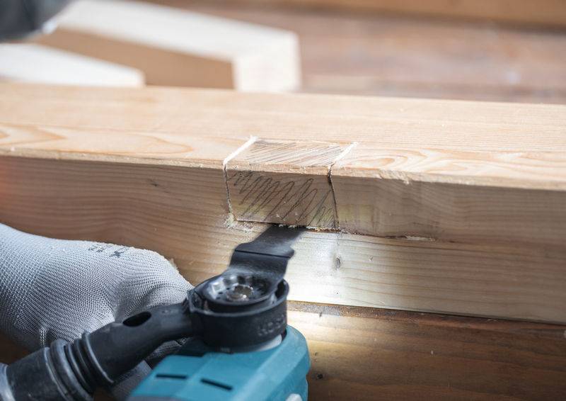 Ein Elektrowerkzeug mit rotierendem Blatt schneidet einen rechteckigen Abschnitt in einen Holzbalken, was Zimmerhandwerk demonstriert.