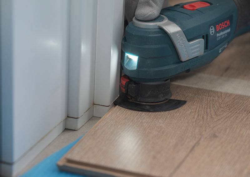 Ein Elektrowerkzeug wird verwendet, um Laminatboden in der Nähe eines Türrahmens zu schneiden, mit Nahaufnahmefokus auf die Schneidekante und die Laminatoberfläche.