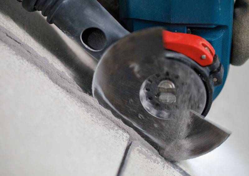 Ein Winkelschleifers schneidet durch eine Fliese und erzeugt dabei Staub. Nahaufnahme, die die Bewegung des Blattes und die Wechselwirkung mit dem Material hervorhebt.