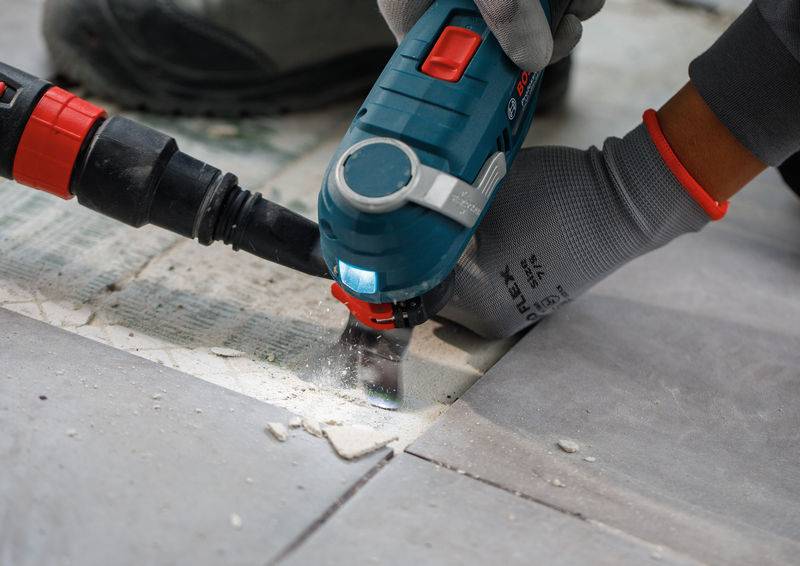 Ein Arbeiter, der mit einem Elektrowerkzeug Bodenfliesen schneidet, trägt Schutzhandschuhe und zeigt präzise, sorgfältige Arbeit in einer Renovierungsumgebung.