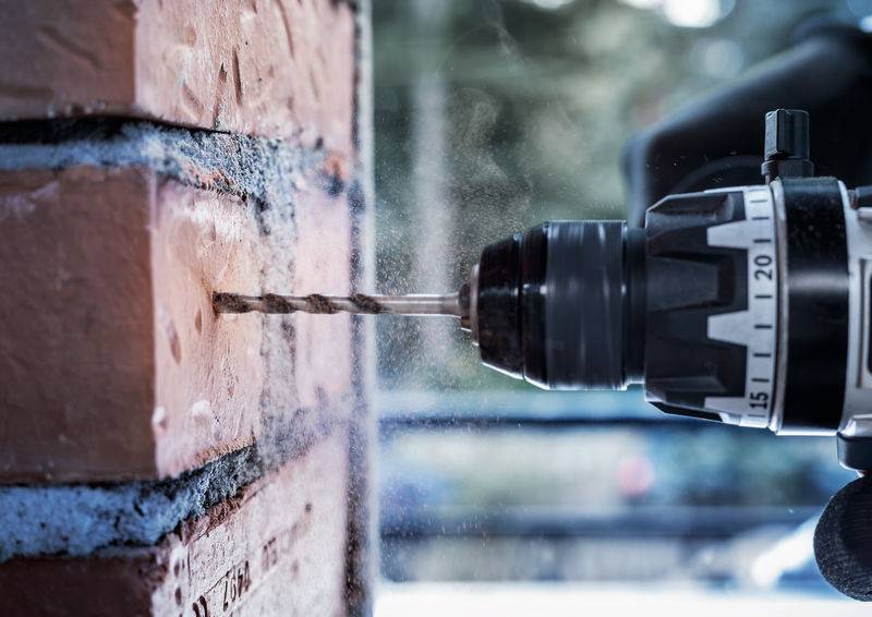 Ein Elektroschrauber bohrt in eine Ziegelmauer und erzeugt dabei Staub. Die Skalierungszahlen des Bohrers sind sichtbar und zeigen die Geschwindigkeitseinstellungen an.