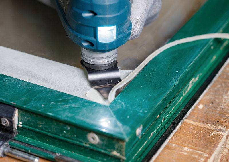 Ein Elektrowerkzeug wird verwendet, um die Kante einer grünen Holzoberfläche umzuformen oder abzuschleifen, wobei ein weißes Kabel daneben auf einem Holzboden liegt.