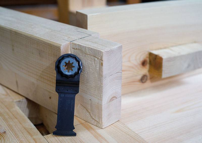 Ein schwarzes Werkzeug, das an einem Holzbalken mit einem teilweise zusammengesetzten Zapfenloch angehängt ist, im Hintergrund. Der Fokus liegt auf der Holzbearbeitungsmontage.