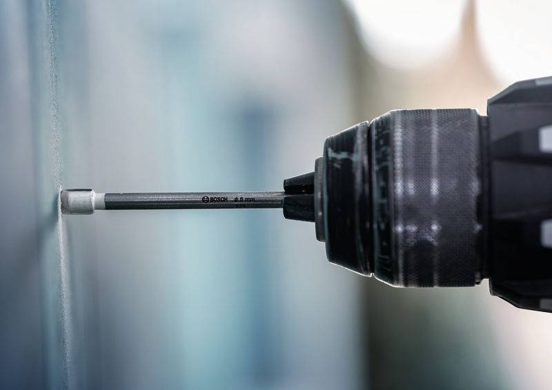 Ein Nahaufnahmebild eines Bohrers mit eingespanntem Aufsatz, positioniert gegen eine glatte Oberfläche, bereit zum Bohren. Die Szene deutet auf laufende Bau- oder Reparaturarbeiten hin.