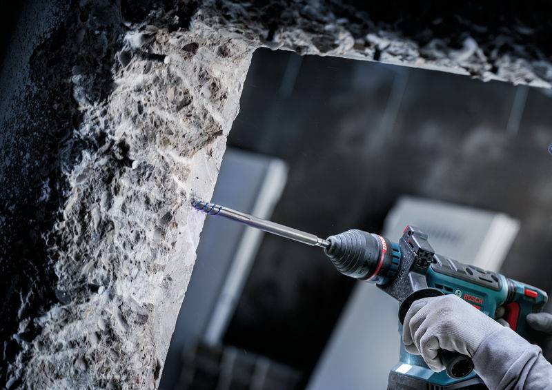 Eine Person in Arbeitshandschuhen nutzt eine Elektrobohrmaschine, um an einer rauen Steinmauer zu arbeiten und konzentriert sich auf eine einzelne Stelle für Präzision.