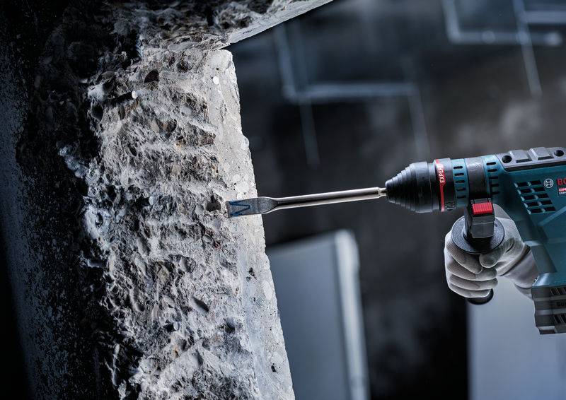 Ein Bohrgerät wird verwendet, um in eine Betonwand zu meißeln, was die Kraft des Werkzeugs bei Bau- oder Abbrucharbeiten demonstriert.