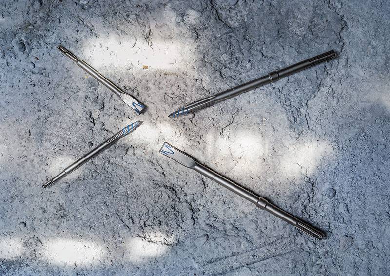 Vier metallische chirurgische Instrumente mit strukturierten Griffen und scharfen Spitzen auf einer strukturierten grauen Oberfläche angeordnet, die weiche Schatten werfen.