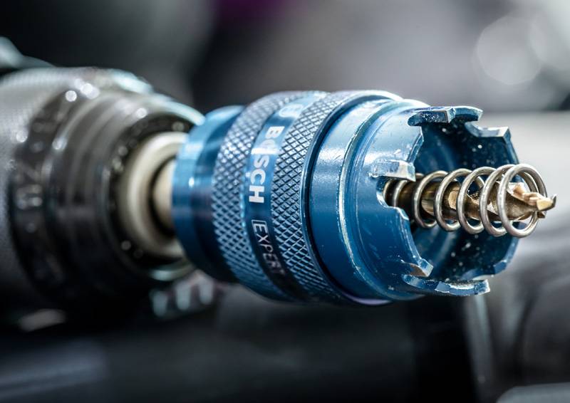 Ein Nahaufnahme einer Elektrobohrmaschine mit einem blauen Metallbohrfutter mit der Beschriftung „BOSCH EXPERT