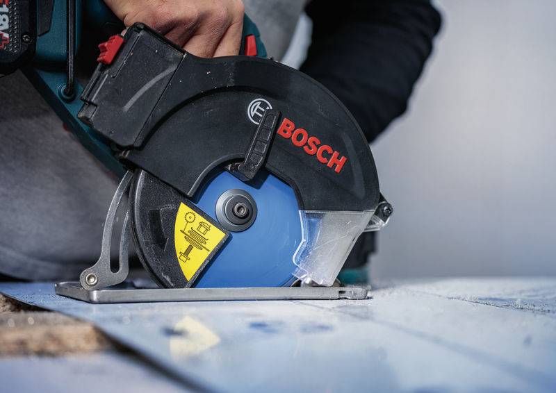 Eine Person verwendet eine Bosch-Kreissäge mit einem blauen Blatt, um durch ein Holzbrett zu schneiden. Die Säge ist für präzises Schneiden angewinkelt.