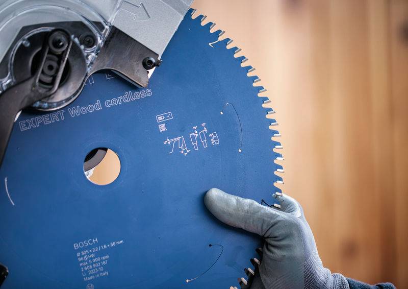 Eine behandschuhte Hand hält ein Kreissägeblatt mit der Aufschrift „EXPERT Wood cordless