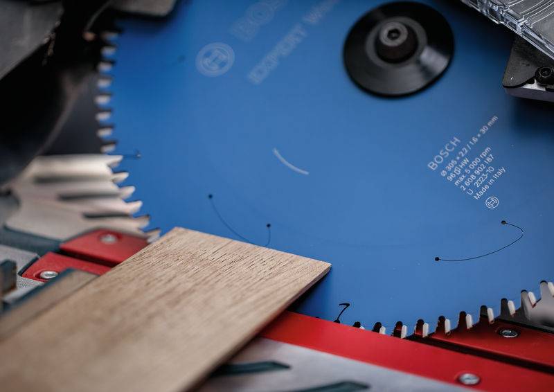 Eine Nahaufnahme einer Kreissägeblatt, das ein Holzstück schneidet. Das blaue Blatt zeigt Markendetails. Die Szene deutet auf eine Holzbearbeitungsaktivität hin.