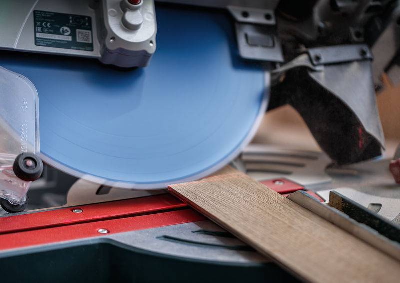 Eine Kreissäge mit einem blauen Blatt schneidet ein Stück Holz durch, wobei die Präzision in der Holzbearbeitung in einer Werkstattumgebung hervorgehoben wird.