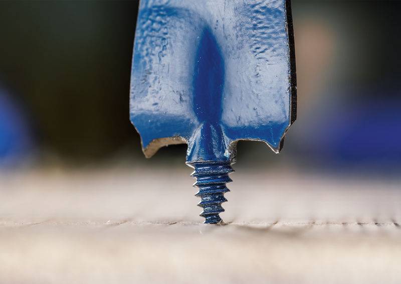 Nahaufnahme der Spitze eines blauen Bohrers mit einem angebrachten Schraubenkopf, vertikal auf einer strukturierten Oberfläche positioniert.