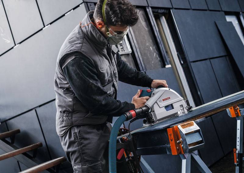 Ein Bauarbeiter in Schutzausrüstung benutzt eine Kreissäge, um einen Metallträger auf einer Baustelle durchzuschneiden.