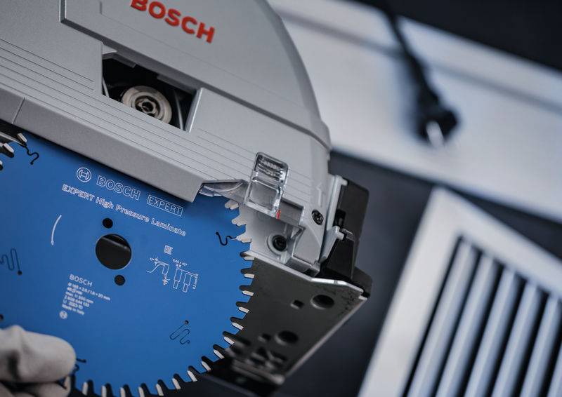 „Nahaufnahme einer Hand, die ein blaues Bosch-Sägeblatt hält, das an einer Kreissäge befestigt ist. Das Blatt ist mit technischen Spezifikationen gekennzeichnet.