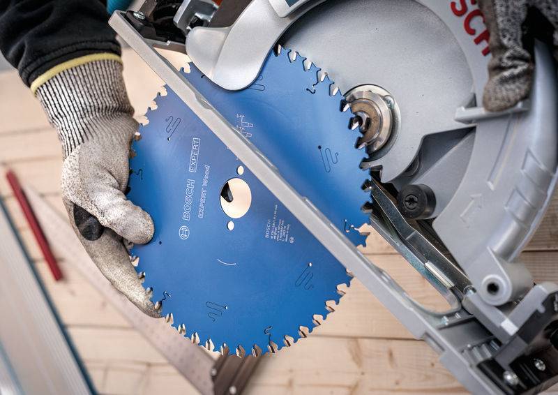 Eine Person mit Handschuhen setzt ein blaues rundes Sägeblatt in eine Elektrosäge ein und bereitet sich auf eine Holzbearbeitungsaufgabe vor.