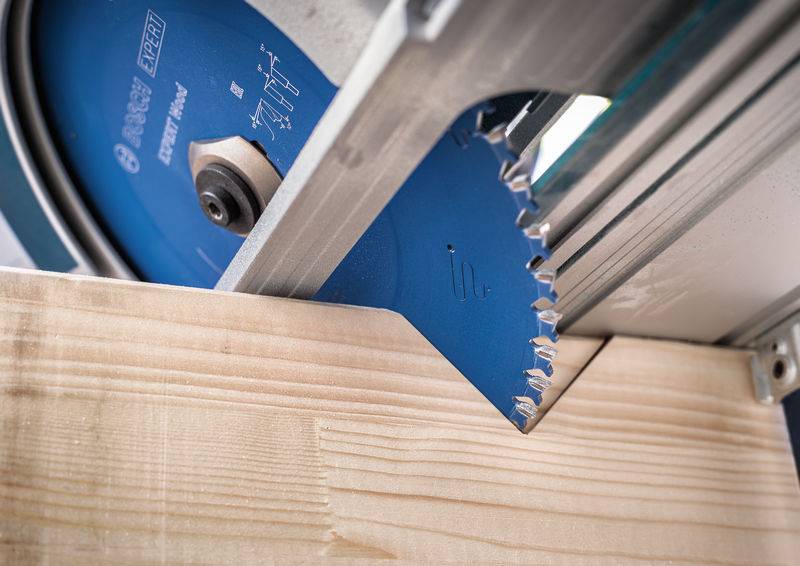 Eine Nahaufnahme einer blauen kreisförmigen Sägeblattscheibe, die durch ein Stück helles Holz schneidet und scharfe Zähne zeigt, die in das Material eindringen.