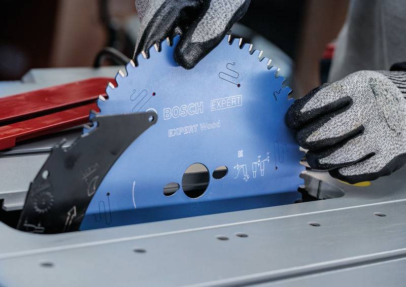 Person mit Schutzhandschuhen installiert ein Bosch Expert Kreissägeblatt. Das Blatt ist blau mit Beschriftungen, die angeben, dass es für das Schneiden von Holz ausgelegt ist.