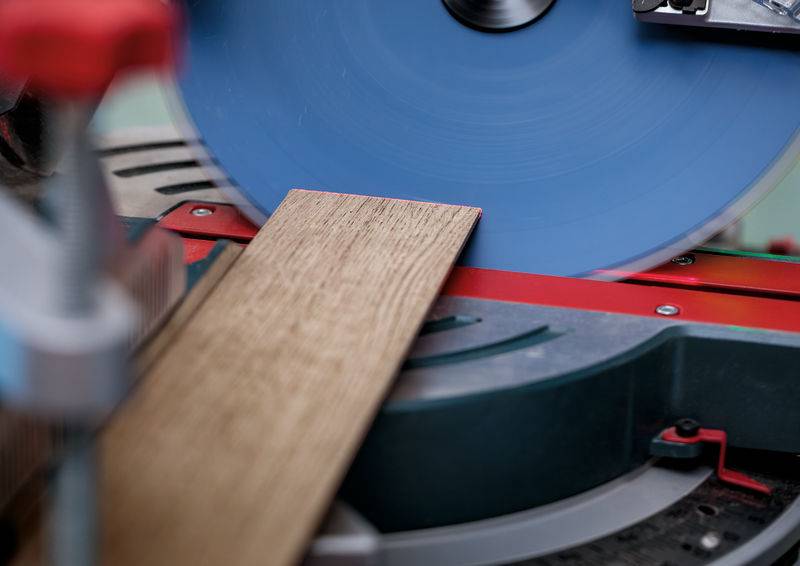 Ein Holzbrett wird von einer Kreissäge geschnitten. Das Sägeblatt dreht sich, und das Brett ist diagonal positioniert und hebt die Holzbearbeitung hervor.