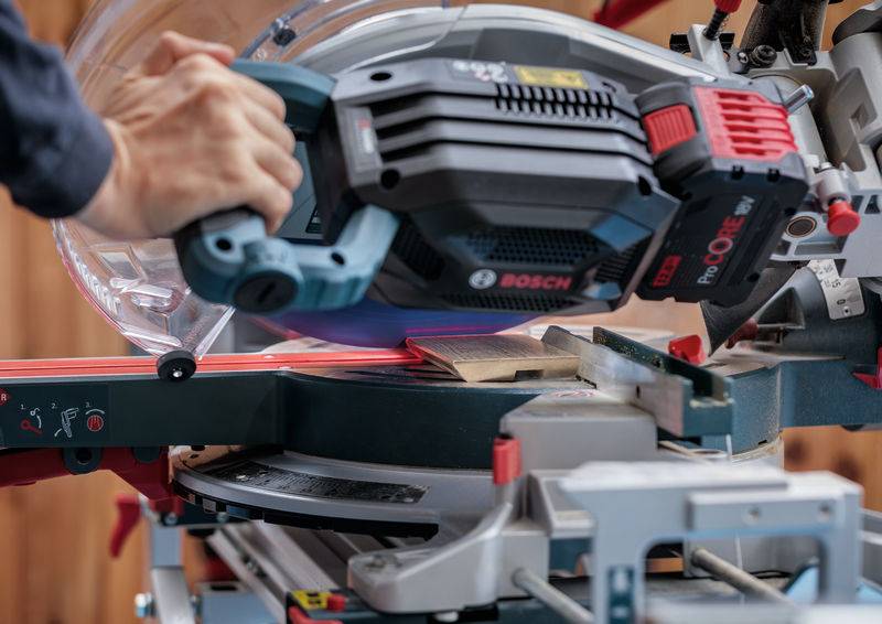 Eine Person benutzt eine Schiebekombinations-Gehrungssäge zum Schneiden eines Holzstücks und demonstriert die Verwendung von Elektrowerkzeugen in der Holzbearbeitung.