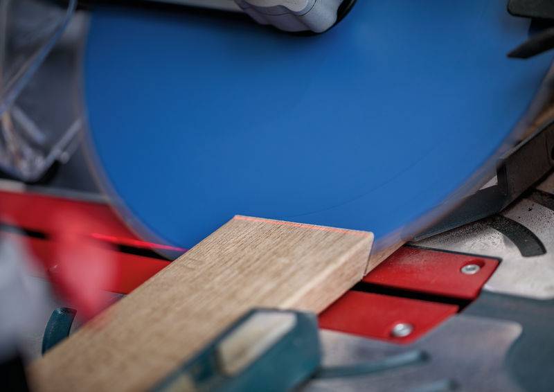 Eine Kreissäge mit einem blauen Blatt schneidet ein Stück Holz auf einem Gehrungssägetisch, was zeigt, dass Holzbearbeitung im Gange ist.