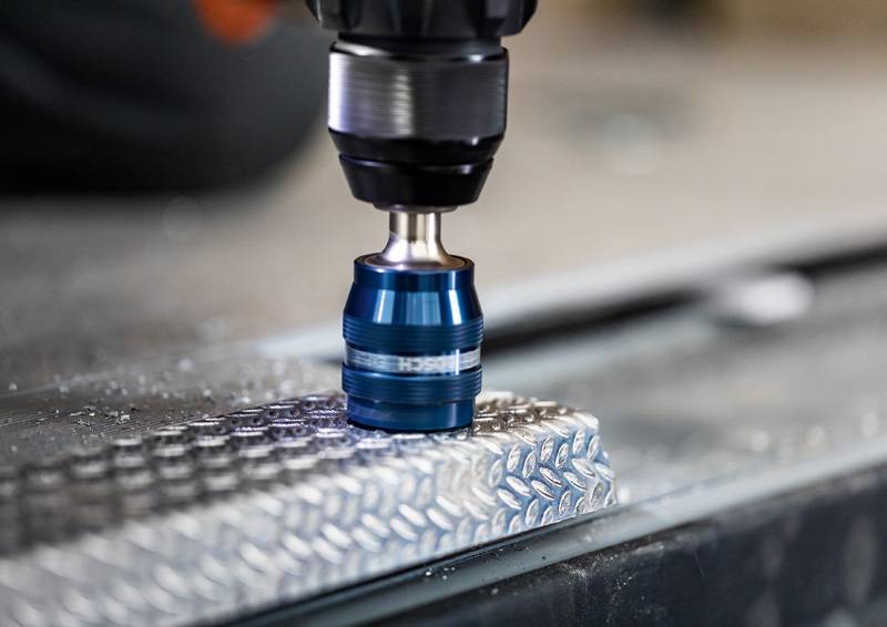 Eine Nahaufnahme eines blauen Bohrers in Betrieb, der in eine strukturierte Metalloberfläche eindringt, mit silbernen Spänen, die um den Bereich sichtbar sind.