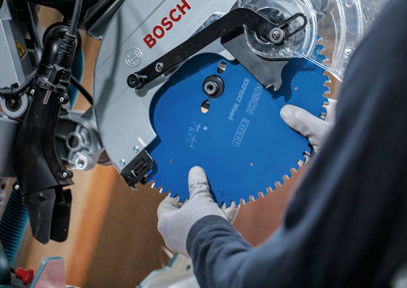 Eine Person mit Handschuhen montiert ein blaues kreisförmiges Sägeblatt auf eine Bosch-Sägenmaschine und konzentriert sich dabei auf Präzision und Sicherheit.