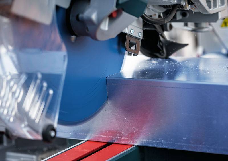 Eine Nahaufnahme eines Industrie-Sägeblatts, das durch ein dickes Metallblech schneidet, wobei Maschinen verwendet werden, die in der Metallfertigung zum Einsatz kommen.