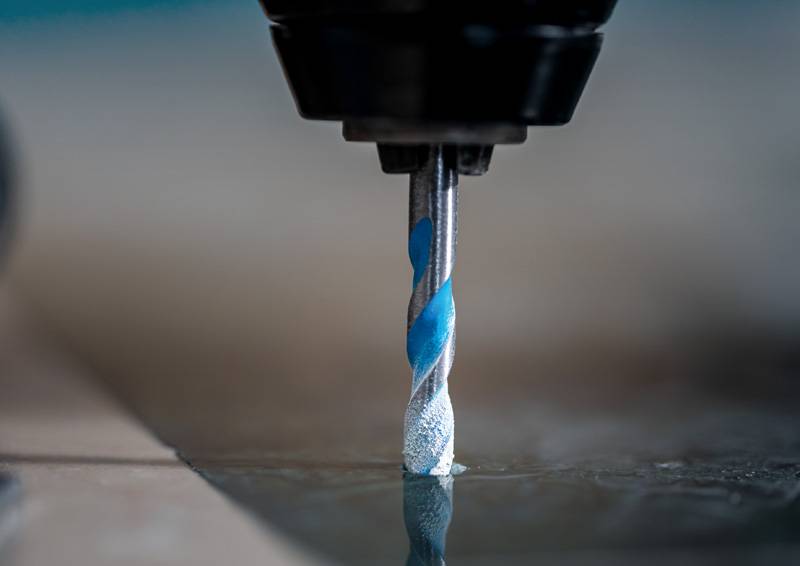 Eine Nahaufnahme eines rotierenden Bohrers mit blauen Akzenten, der in eine metallische Oberfläche eindringt, mit unscharfem Hintergrund zur Betonung des Bohrers.