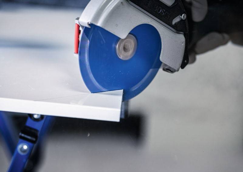 Eine Kreissäge mit einem blauen Blatt schneidet durch ein Stück weißes Material auf einer Werkbank und veranschaulicht einen präzisen Schneidprozess.