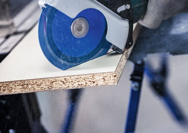 Eine Nahaufnahme einer Kreissäge, die durch ein Stück Holz schneidet, zeigt Staubpartikel in der Luft und demonstriert einen Holzbearbeitungsprozess.