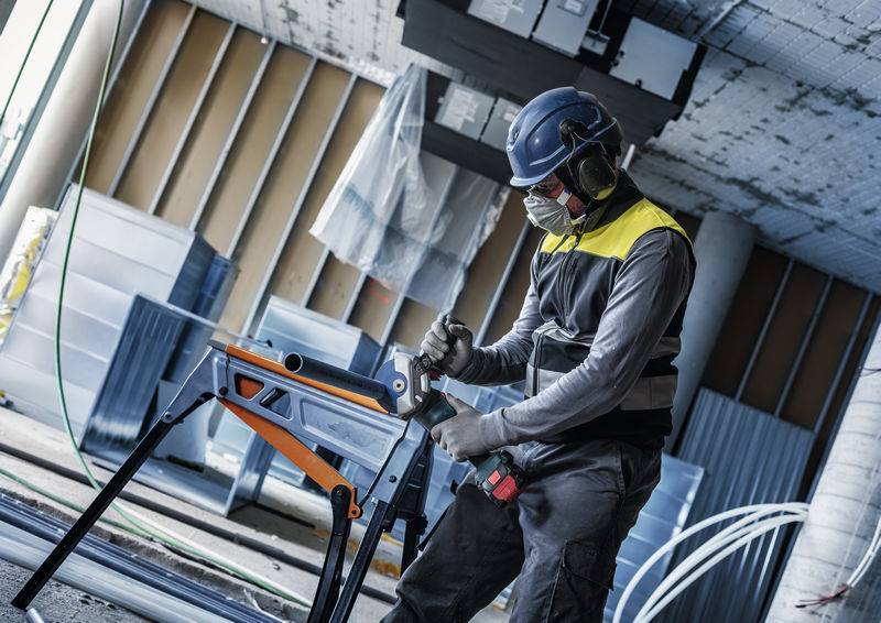 Ein Bauarbeiter in Schutzausrüstung verwendet eine Säge, um Materialien in einem teilweise errichteten Gebäude zu schneiden.